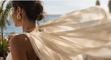 Mulher de costas com vestido claro esvoaçante, à beira-mar